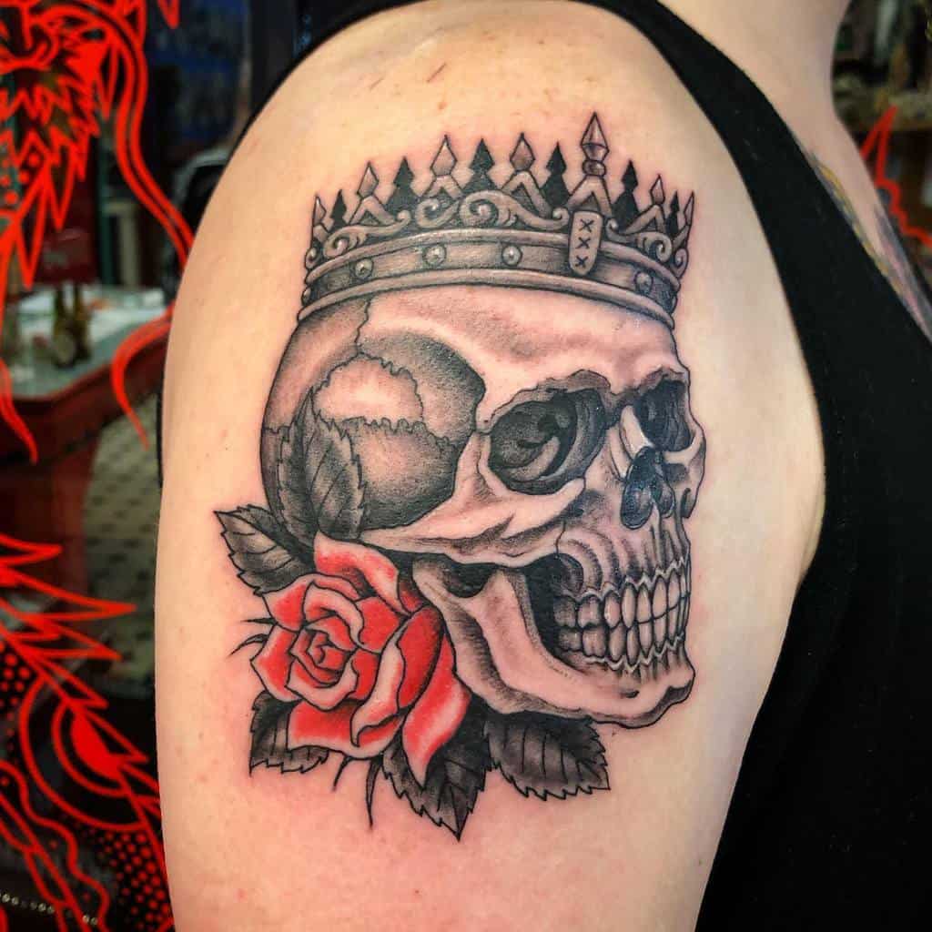 Black and grey tattoo of a crowned skull with a red rose, symbolizing power and mortality, detailed with bold shading on the upper arm.