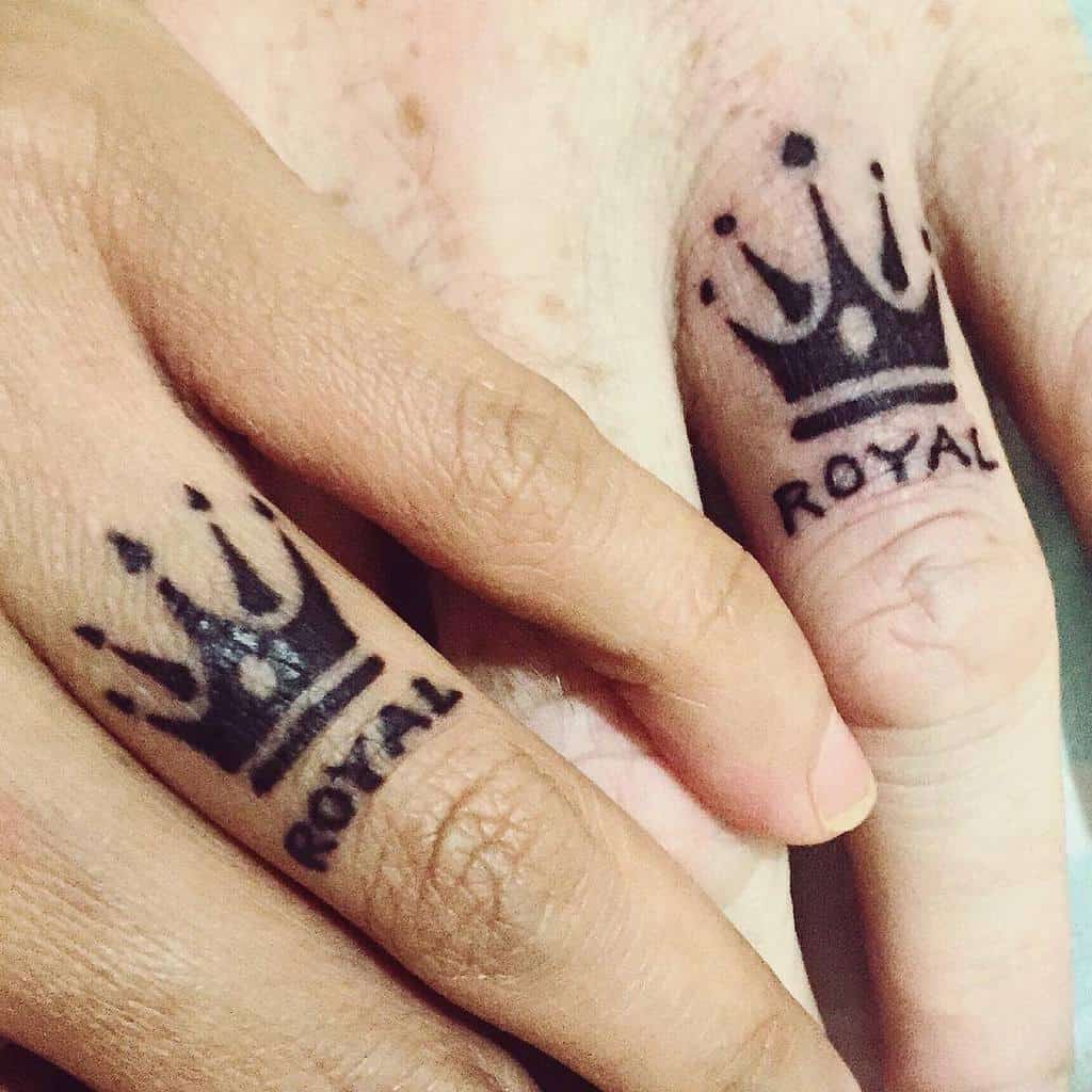 A matching wedding ring tattoo of crowns with the word "ROYAL" underneath each, placed on two fingers to symbolize a strong, united connection
