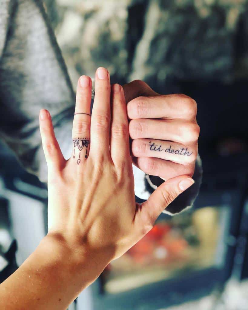 A matching wedding tattoo set with mandala design crown on one finger and the phrase "'til death" on the other
