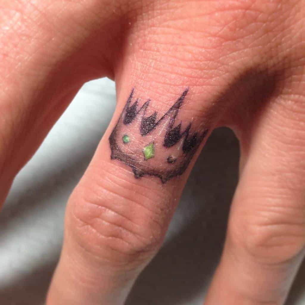 A wedding ring tattoo of a crown with green gemstones on the finger, designed with a minimalist, sharp-edged look