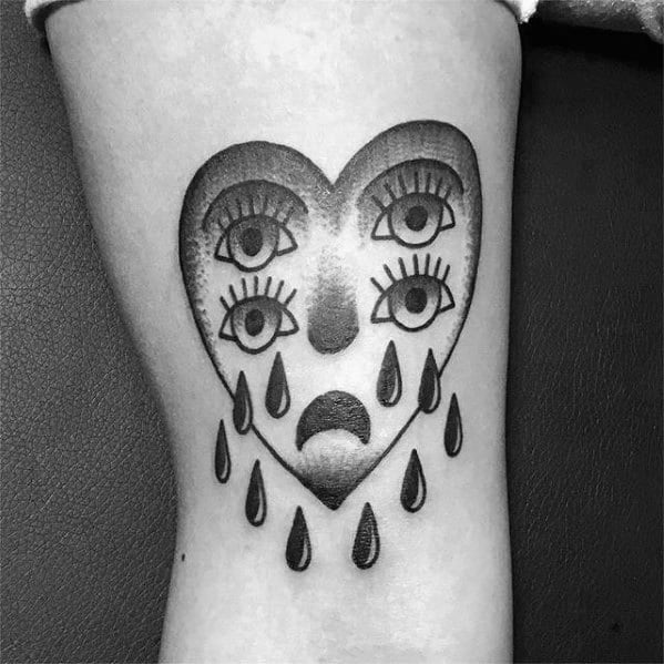 Surreal heart tattoo with multiple eyes, a sad face, and teardrops