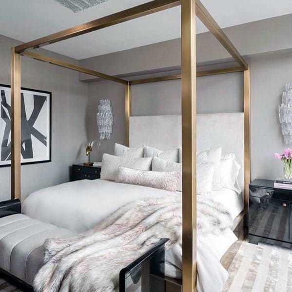 Modern bedroom with gold four-poster bed, cozy bedding, and crystal wall sconces.