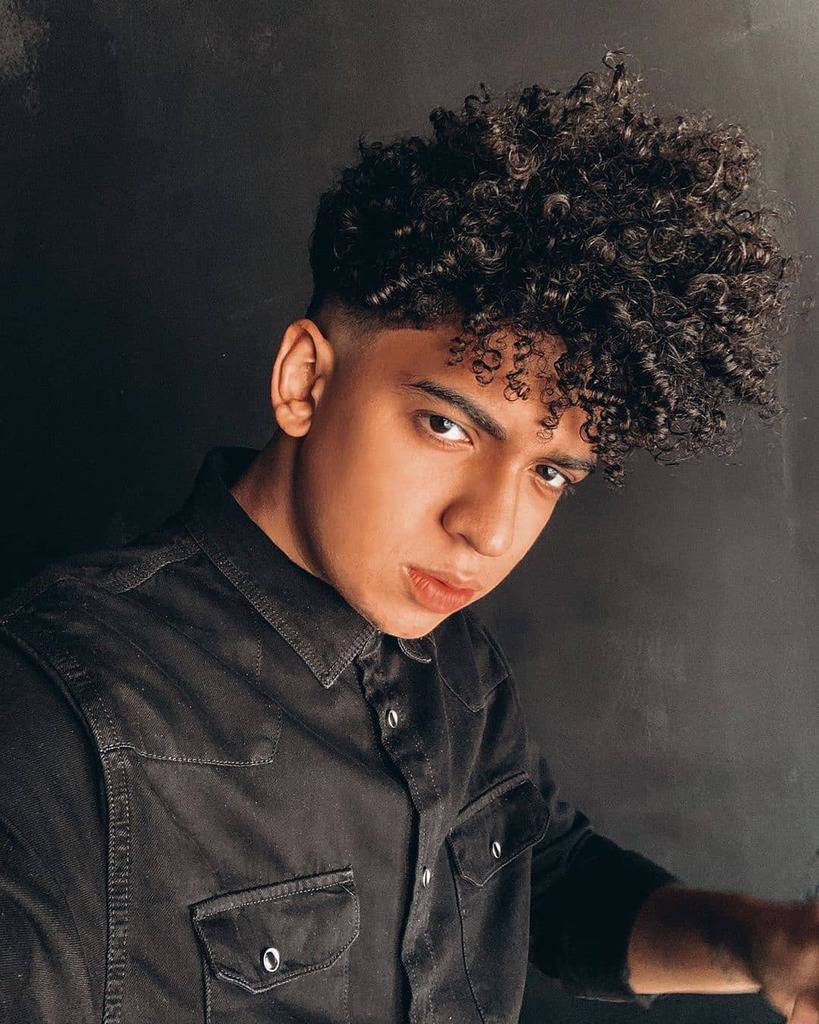 A curly pompadour with long curly hair in front that covers some part of the forehead with short manes on the sides and back