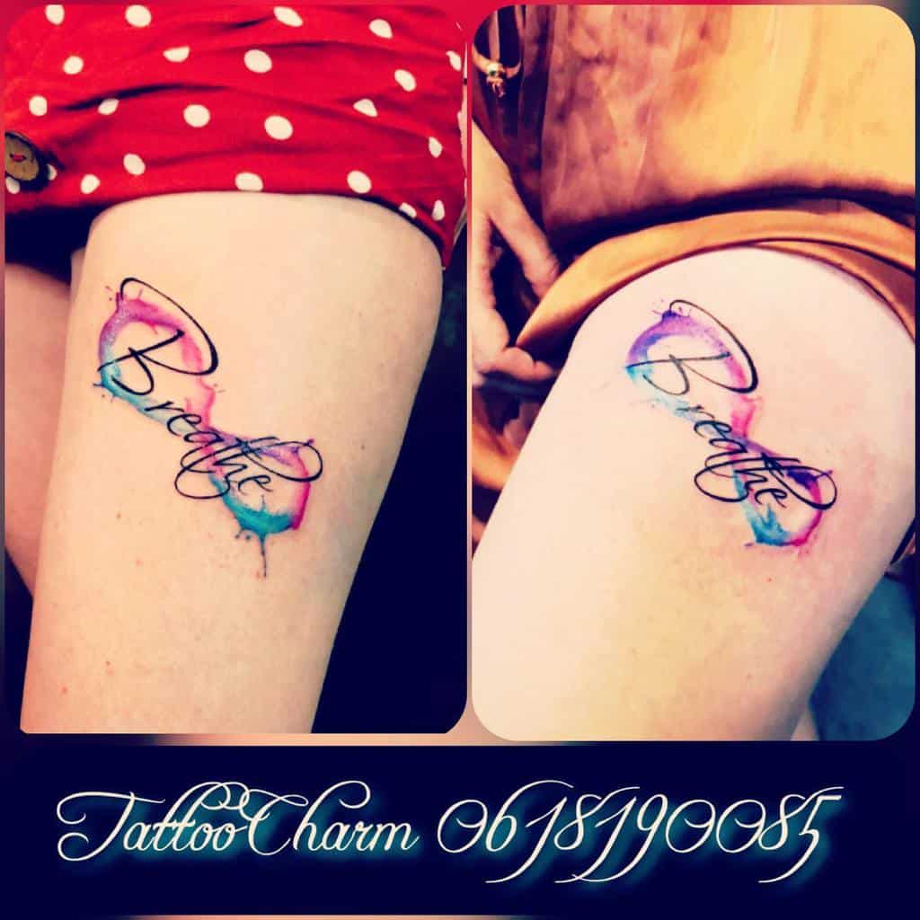 A stunning tattoo of the word "Breathe," elegantly scripted in cursive with a mesmerizing watercolor effect, graces a leg