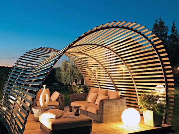 Curved wooden pergola with cozy wicker seating, ambient lighting, and modern outdoor design.