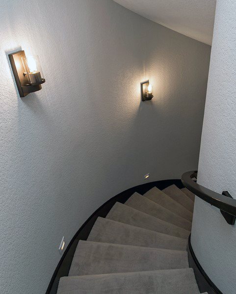 Curved staircase with carpeted steps and wall-mounted lighting in a modern hallway.
