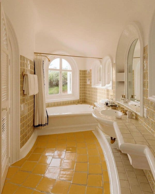 Light-filled bathroom with arch windows, yellow floor tiles, curved edges, and mosaic accents for a Mediterranean feel.