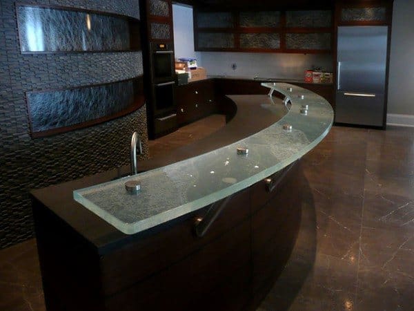 Sleek curved glass bar top with dark wood base and modern fixtures in a contemporary kitchen.