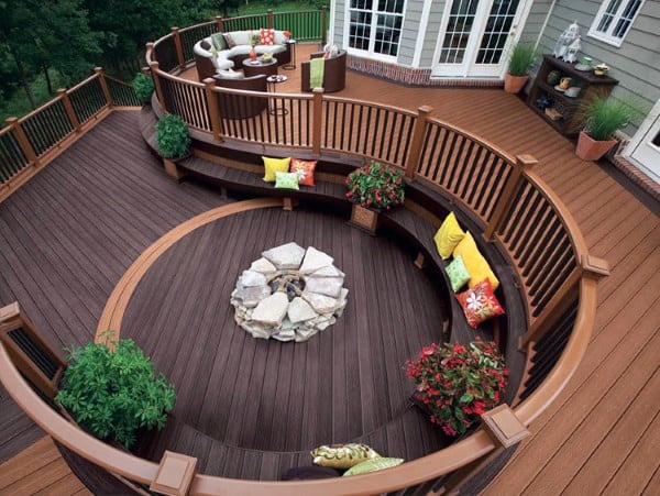Curved multi-level deck with built-in seating, colorful pillows, and a central firepit.