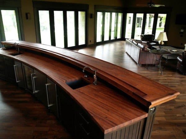 Curved wooden bar top with built-in sink and dark cabinetry in an open living space.