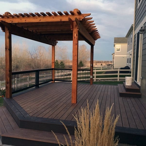 Wooden deck with pergola and railing overlooking a fenced backyard and open landscape.