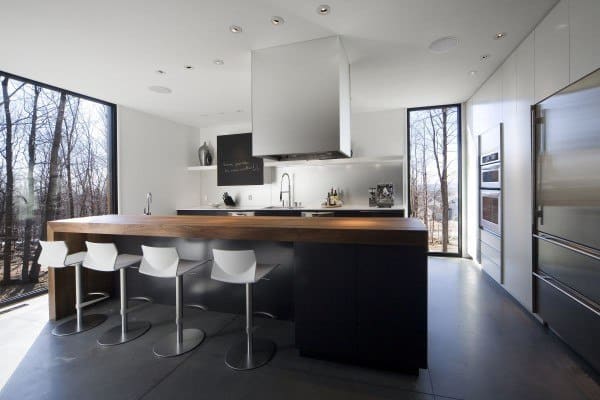 Minimalist kitchen with thick wooden bar top, white bar stools, and large windows.