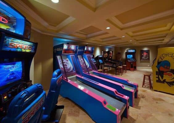 An arcade room with racing and skee ball games, pinball machines, and retro gaming cabinets under soft lighting