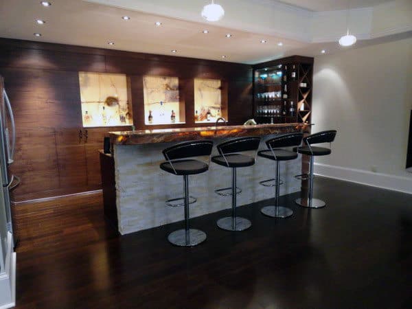 Modern home bar with sleek design, featuring four high stools and backlit shelves showcasing bottles in a dark wood finish