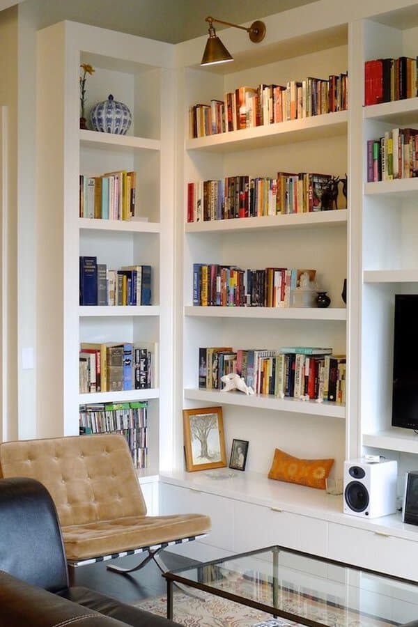White built-in bookshelves with a reading nook, brass wall sconce, and modern seating.