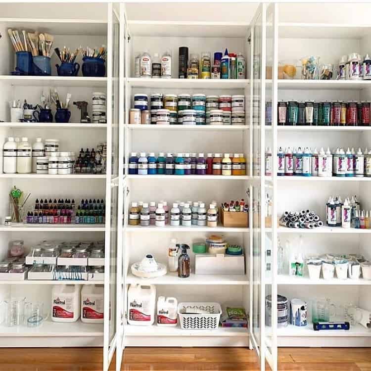 A well-organized shelving unit filled with art supplies, including paints, brushes, and bottles