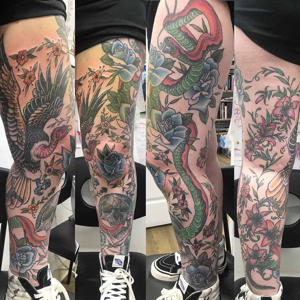 Colorful full leg sleeve tattoo featuring vibrant flowers with leaves, a snake, a skull, and a bird in motion