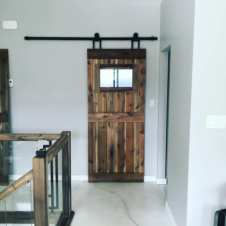 Dark wood sliding barn door with a glass window panel in a modern hallway.