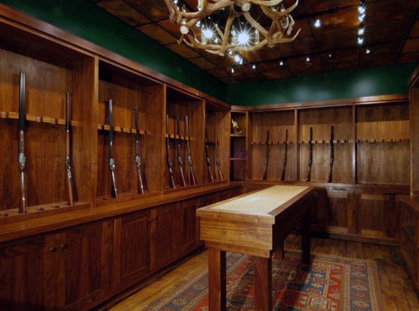 Rustic gun room with custom wood cabinetry, green walls, and antler chandelier. Perfect for collectors.