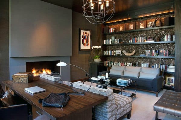Modern living room with a large bookshelf, cozy fireplace, sofa, and wooden desk, creating a mini library feel
