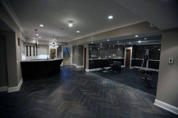 Spacious home basement with a kitchen, wooden herringbone floor, gym equipment, and glass-enclosed area