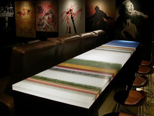 Colorful resin bar top with leather seating and movie poster decor in the background.
