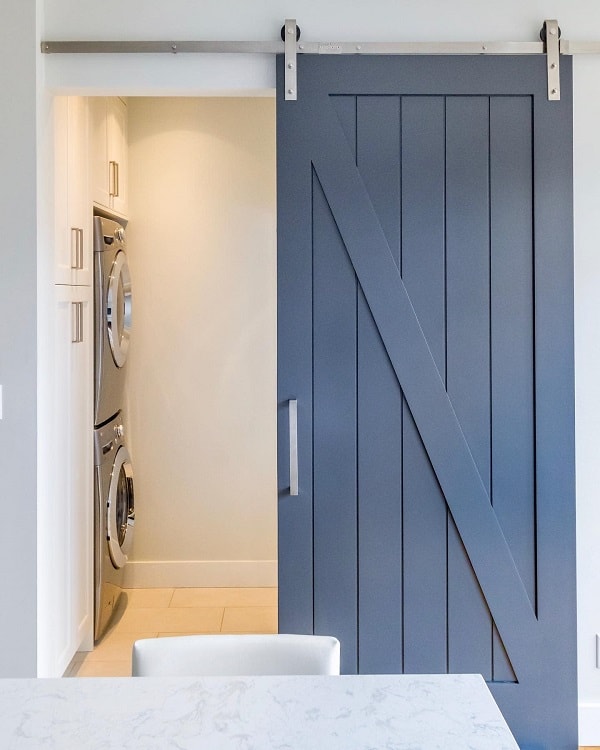 Blue sliding barn door leading to a laundry area with stacked washer and dryer.