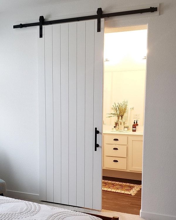 White sliding barn door leading from bedroom to a bright bathroom with a modern vanity.
