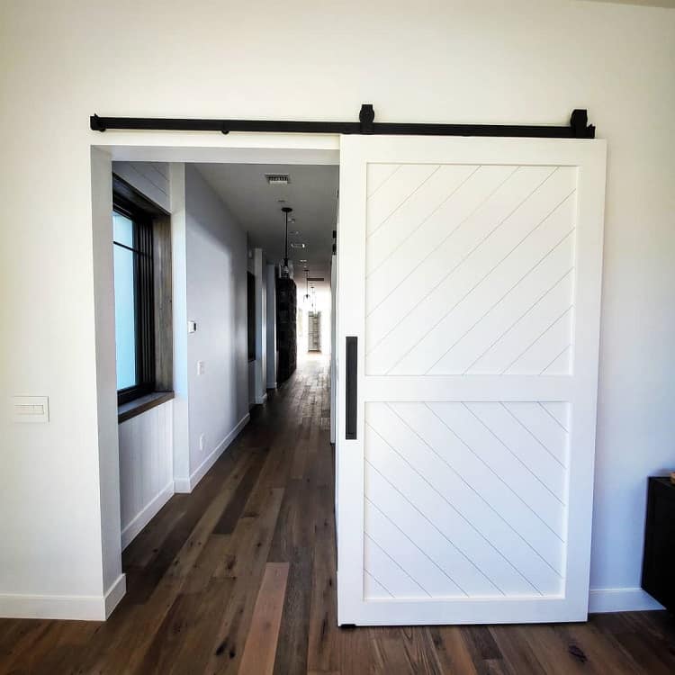 White wood sliding barn door opening to a modern hallway with wooden floors and natural light.