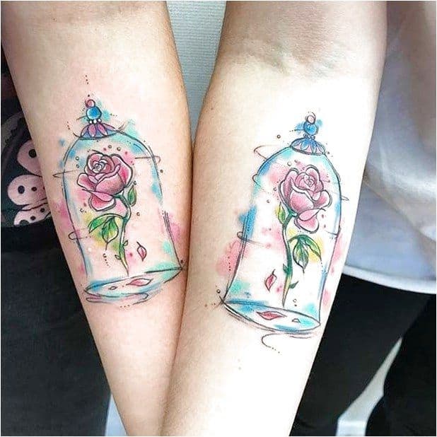 Matching watercolor-style tattoos of the enchanted rose inside a glass dome, featuring soft pink, blue, and green hues with delicate details.
