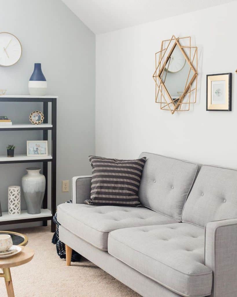 Light grey sofa with a patterned pillow, geometric mirror, decorative bookshelf, and soft neutral accents.