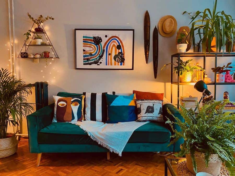 Colorful living room with green velvet sofa, abstract art, vibrant pillows, plants, and cozy lighting.