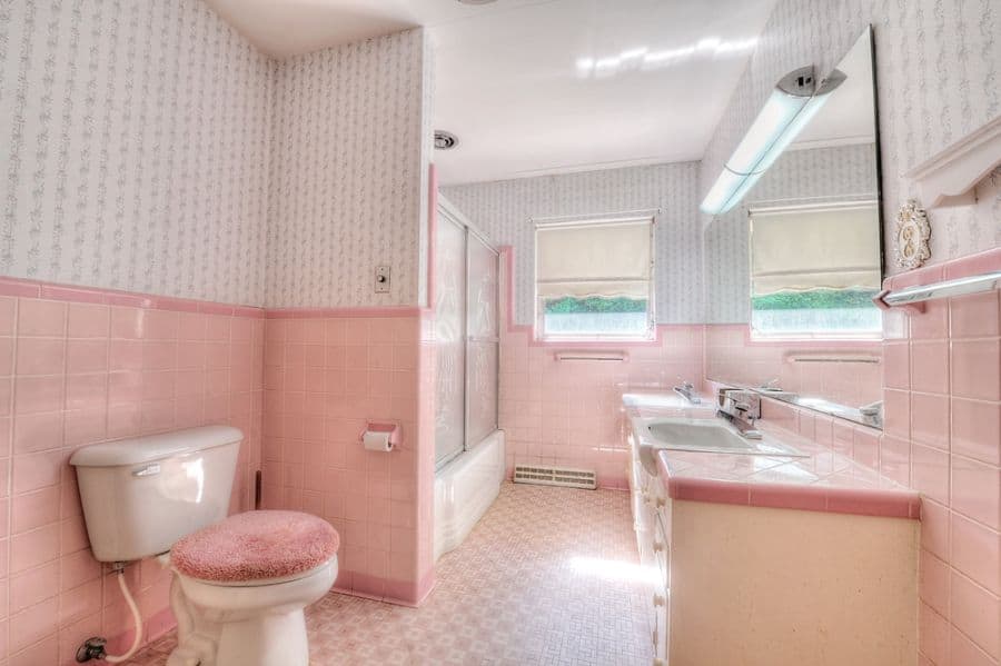 Vintage pink-tiled bathroom with matching sink, bathtub, and patterned wallpaper.