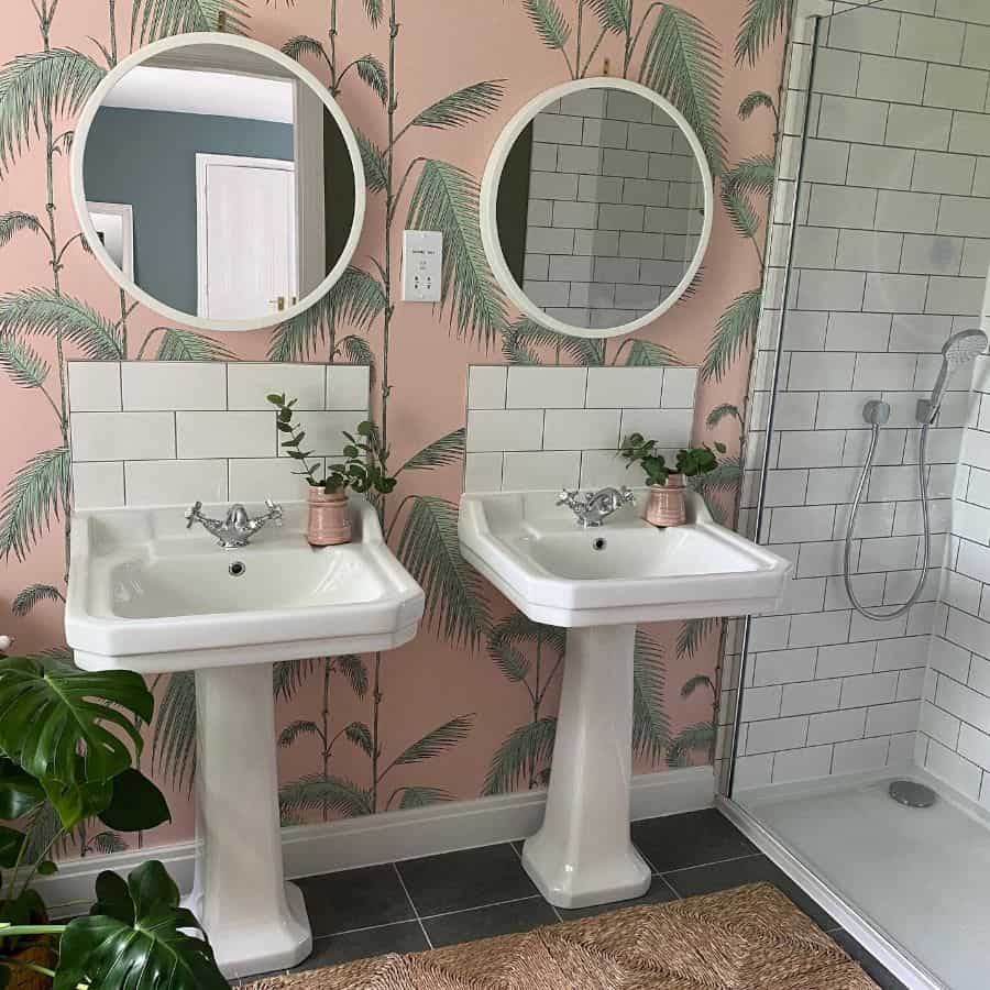 Bathroom with pink palm tree wallpaper, dual pedestal sinks, and round mirrors.