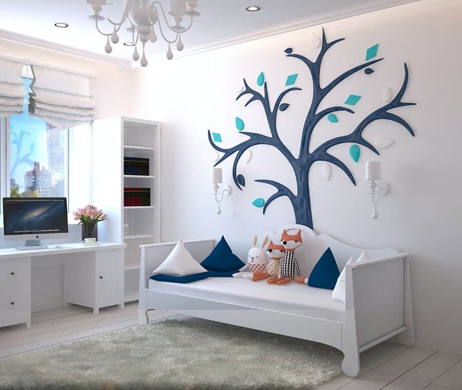 Bright kids' room with a tree wall design, desk with computer, and daybed with plush toys and pillows