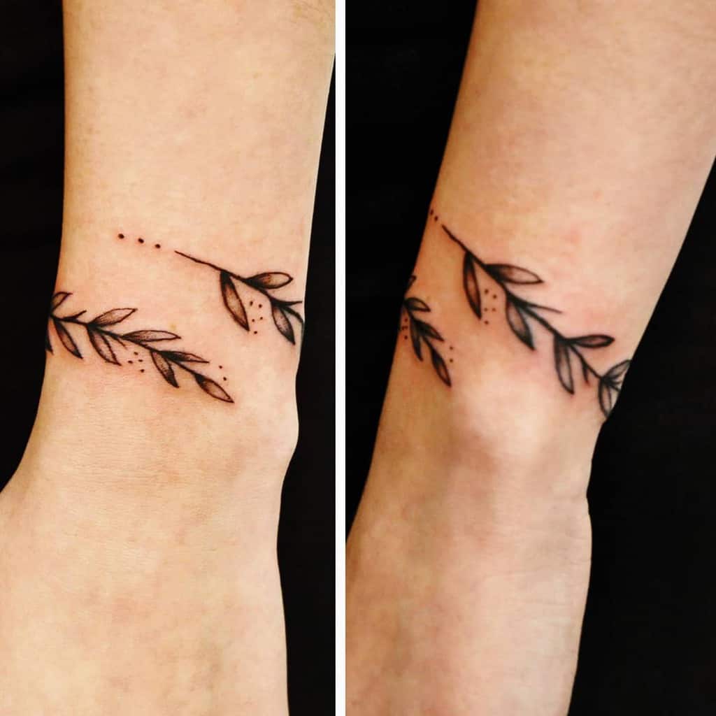 A minimalistic tattoo of a delicate leaf branch with fine details and dots, placed around the wrist.