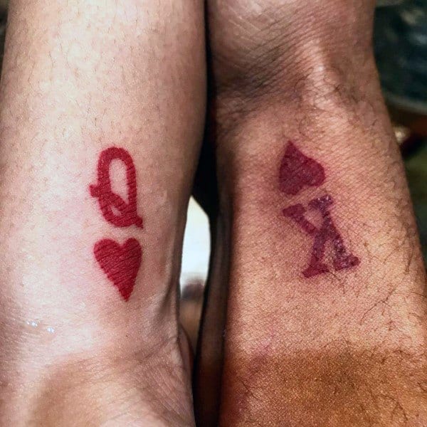 Matching wrist tattoos of a red Queen of Hearts and King of Spades, symbolizing a powerful and loving bond between partners.