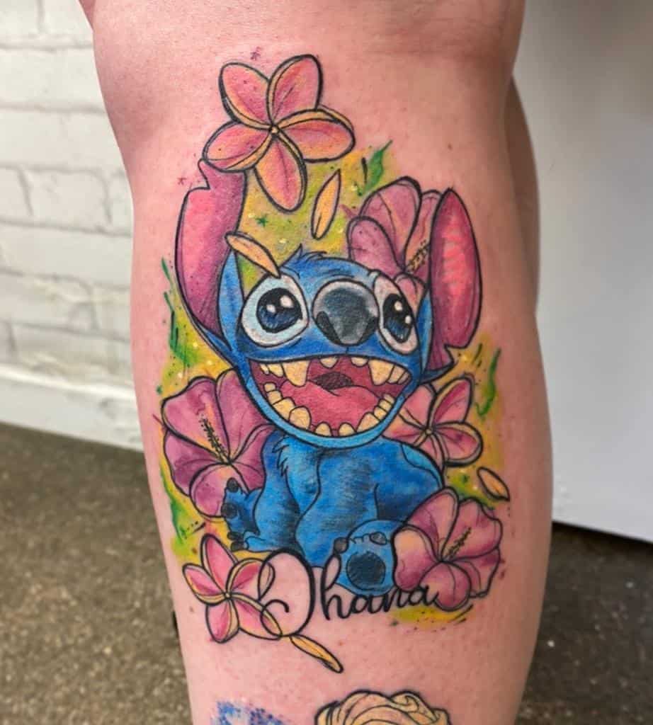 Colorful tattoo of Stitch from Lilo & Stitch with hibiscus flowers and the word 'Ohana' below, on the calf.