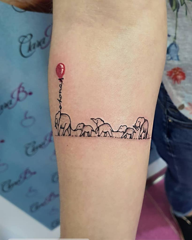 Minimalist 'Ohana' tattoo featuring a family of elephants walking together with a red balloon, symbolizing love, unity, and family bonds.