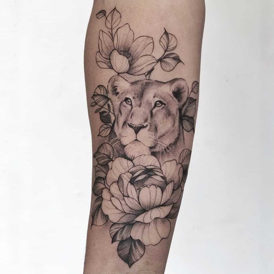 Elegant black and grey lioness tattoo on the forearm, surrounded by detailed peonies and leaves for a soft yet powerful design.