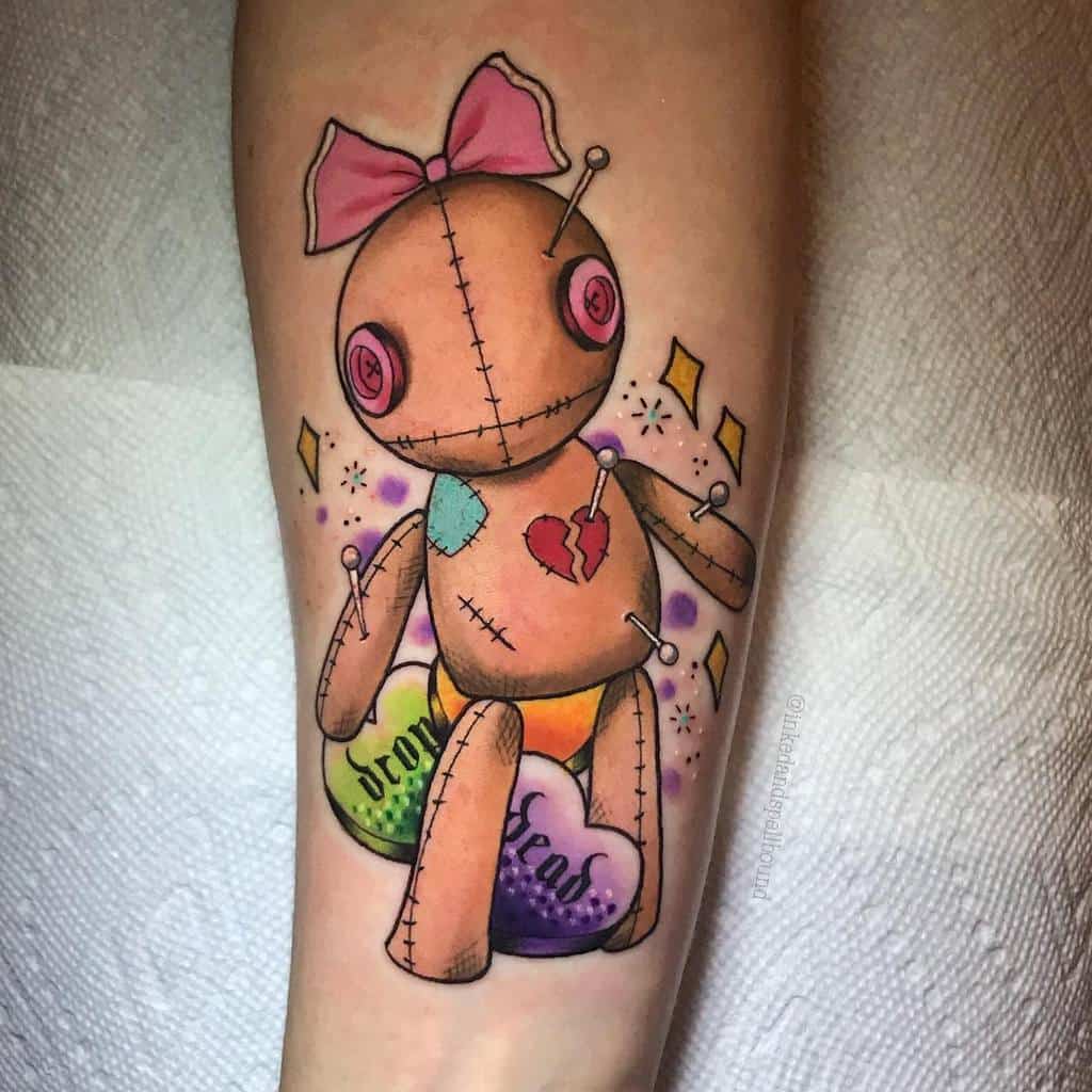 Colorful voodoo doll tattoo with a pink bow, heart patch, pins, and candy hearts labeled 'Drop' and 'Dead'