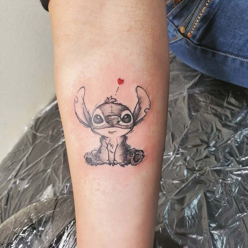 Small black and white tattoo of Stitch from Lilo & Stitch with a red heart above his head.
