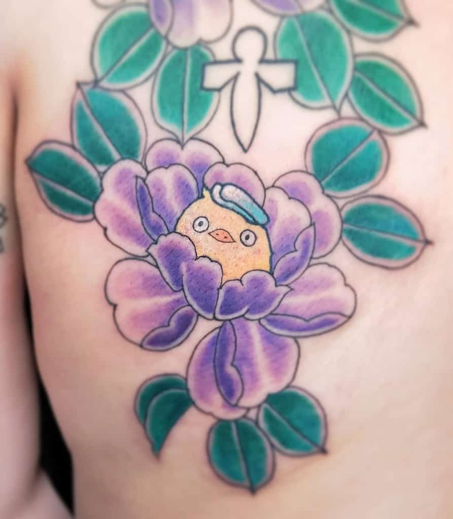 Colorful tattoo of the Spirited Away bathhouse chick peeking from a vibrant purple peony, surrounded by green leaves in a bold style