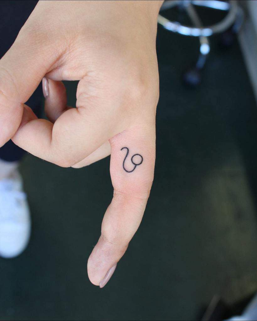 Small and simple Leo zodiac symbol tattooed on the side of the index finger in fine black ink.