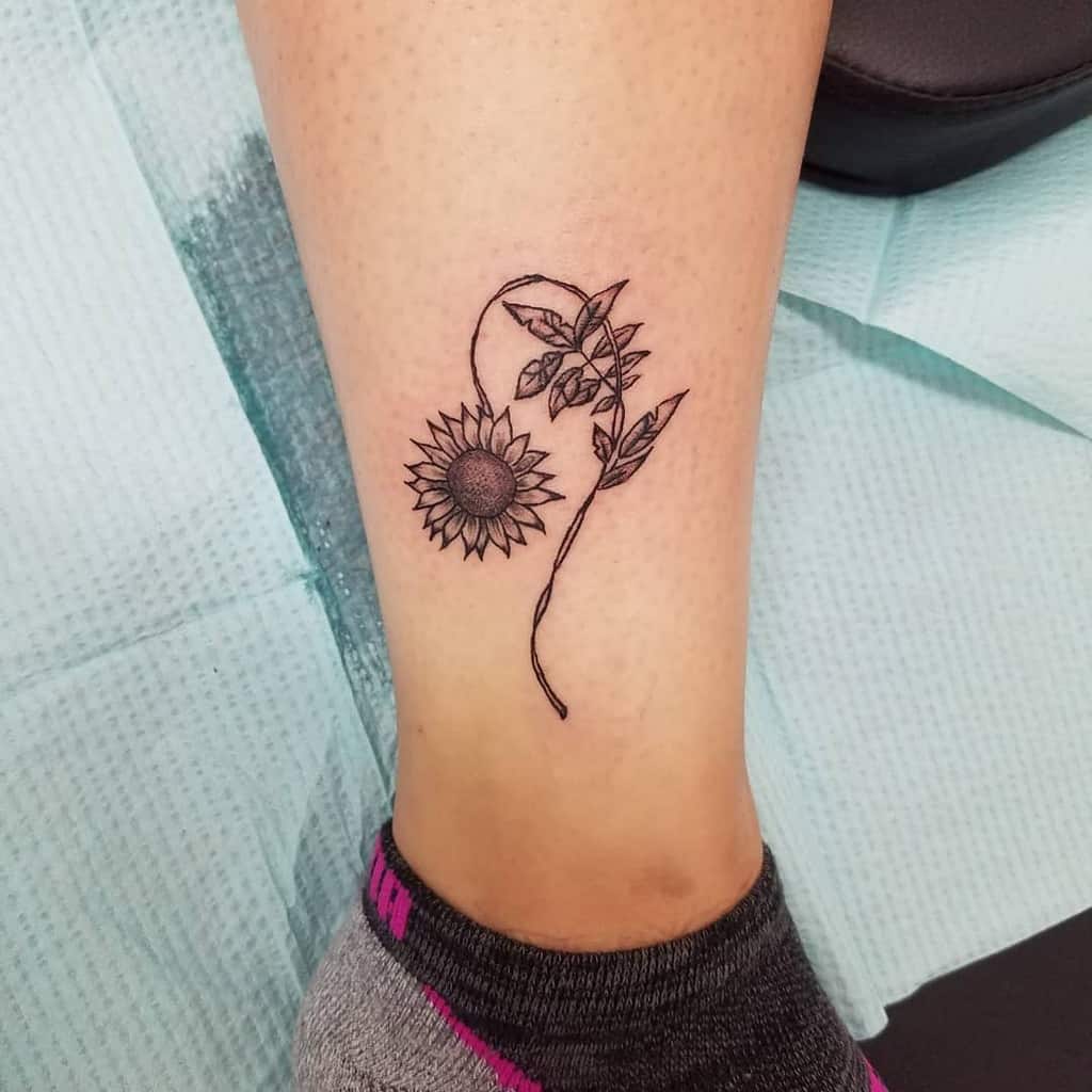 Fine-line sunflower and vine tattoo creating the Leo symbol, representing strength, warmth, and natural beauty.
