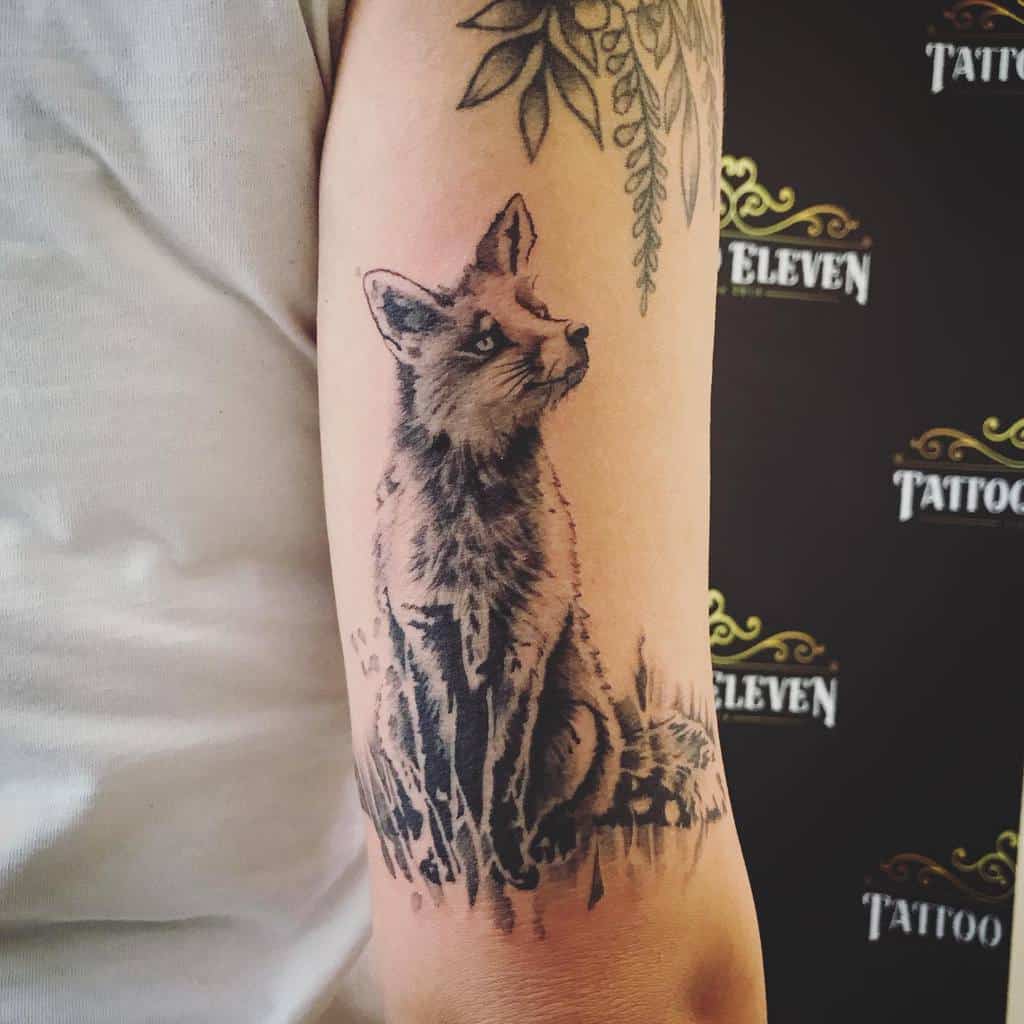 Tattoo of a detailed fox sitting under leaves on a woman's upper arm