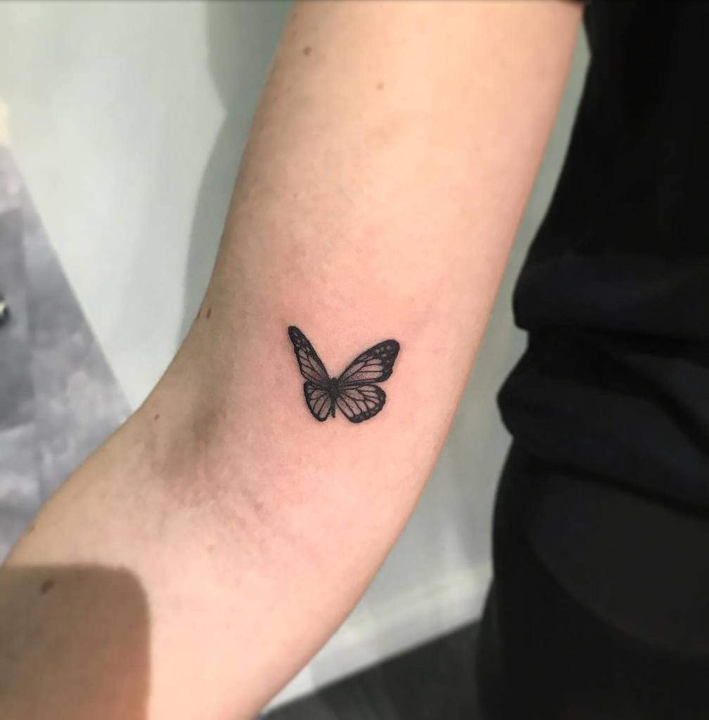 A black ink butterfly tattoo on a person's inner arm, with detailed wing patterns