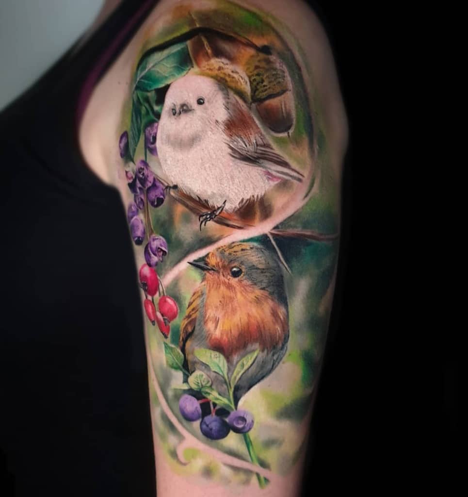 Colorful bird tattoos on a person's arm with upper berries and leaves
