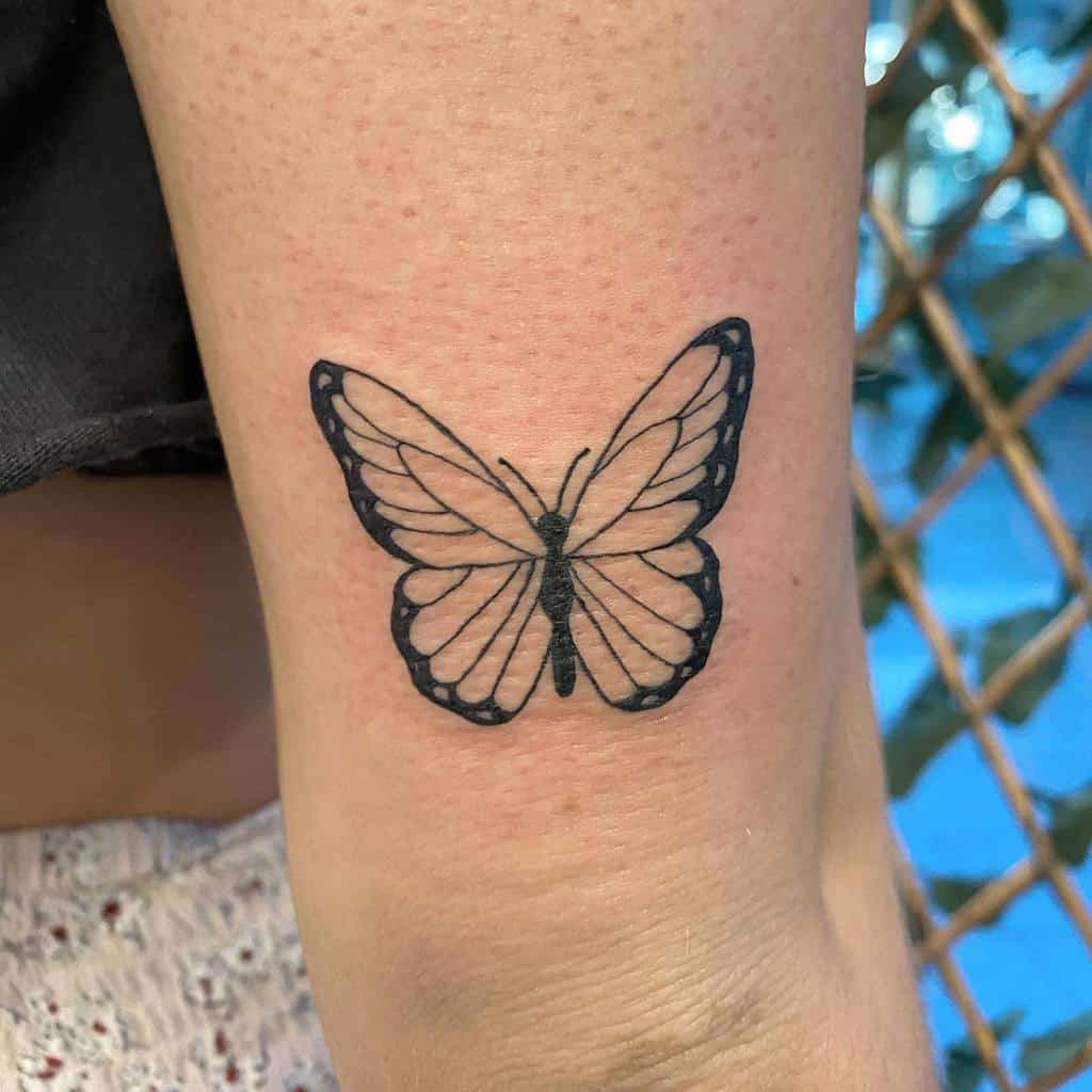 Black outline butterfly tattoo on an upper arm