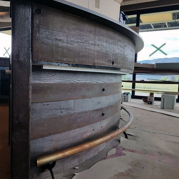 Curved brass foot rail around a rustic wooden bar with a smooth countertop in a modern setting.